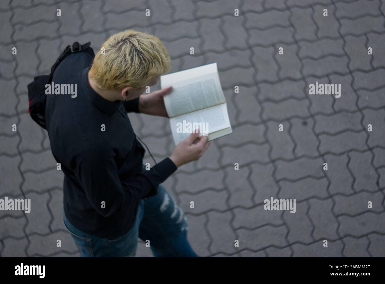 Vue de dessus d'un jeune homme lisant un livre sur le trottoir Banque D'Images