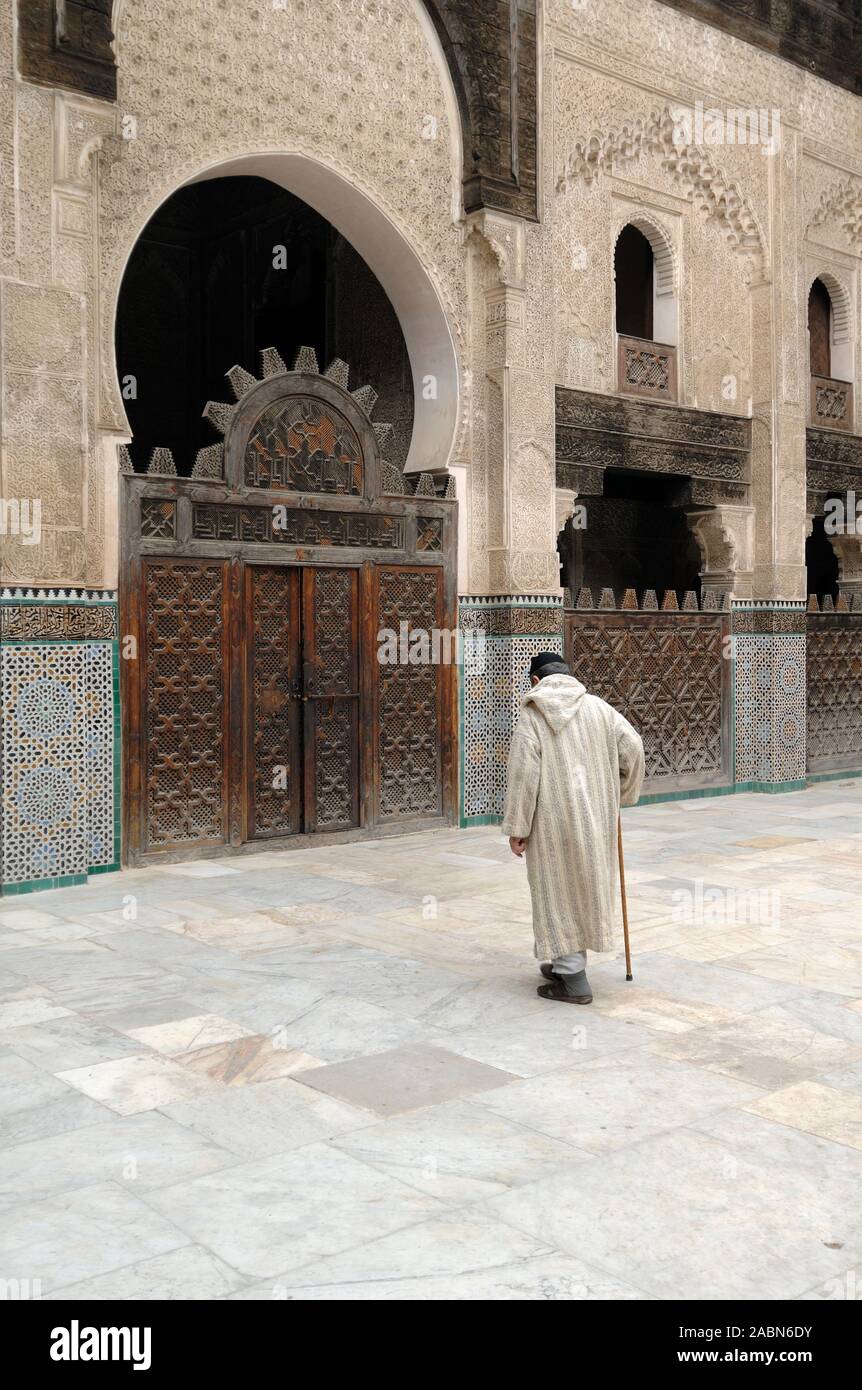 Le vieil homme marocain en vêtements traditionnels marche avec un bâton de marche De l'autre côté de la cour de Bou Inania Medersa (1350-56) Fez Maroc Banque D'Images