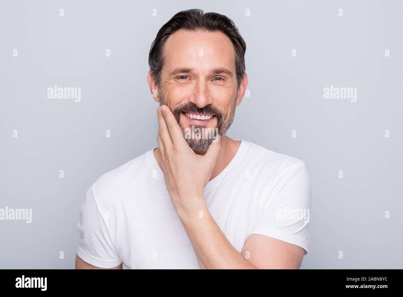 Photo gros plan de bel homme d'âge positif à la main en souriant à pleines dents miroir barbe contrôle après l'utilisation de gel de rasage nouveau porter t-shirt blanc isolé Banque D'Images