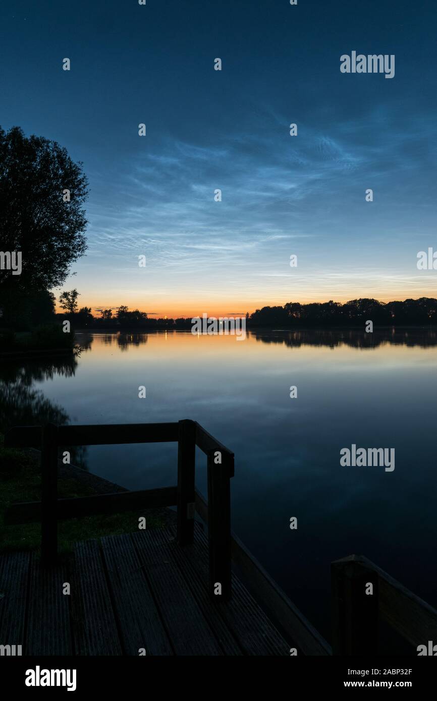 Scène tranquille après le coucher du soleil près de l'eau calme d'un lac avec shining nuit nuages (NLC ou nuages noctilucents) dans le ciel. Banque D'Images