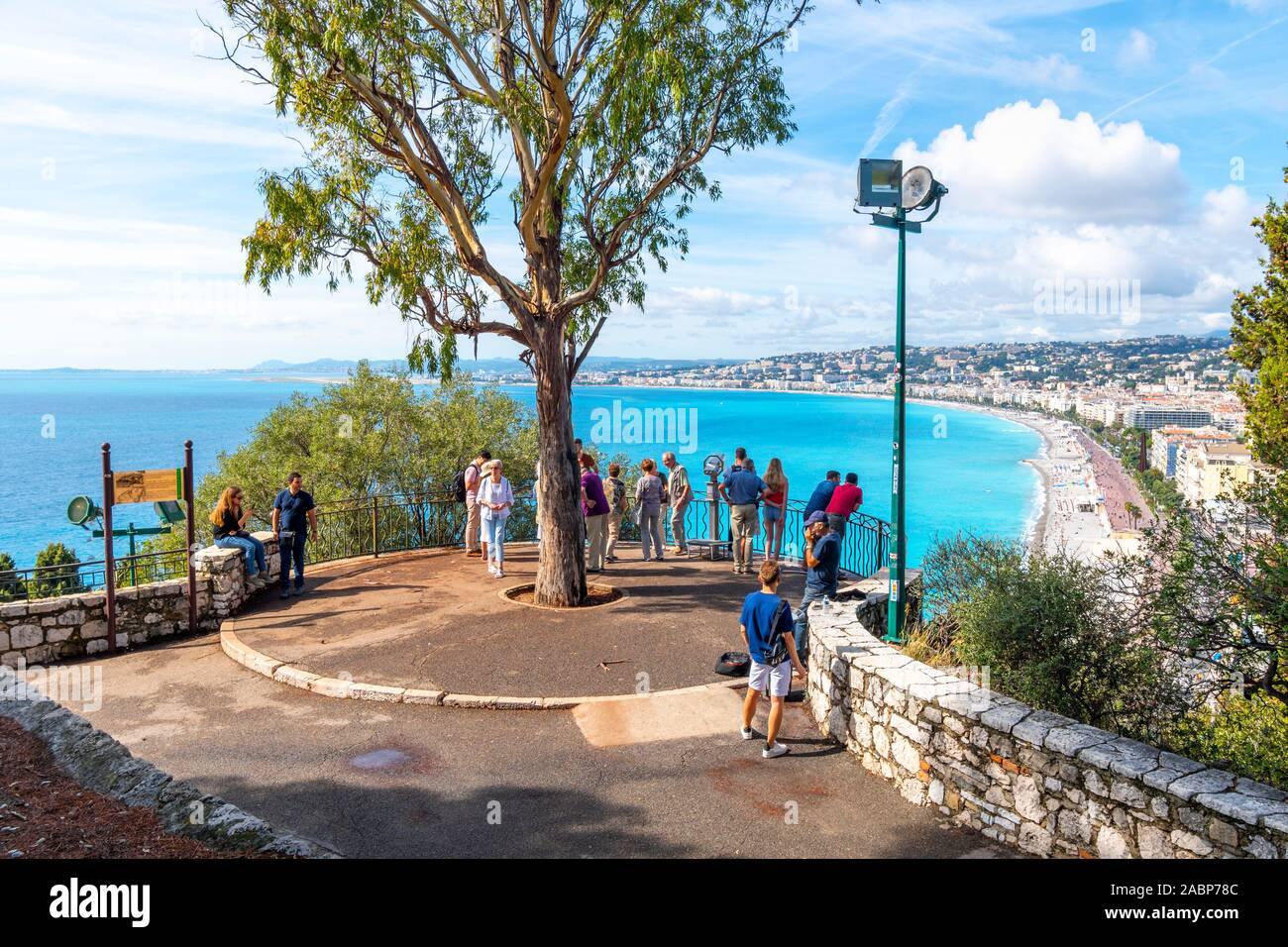 Les touristes visitent la colline du château surplombant les eaux turquoises de la Méditerranée et de la ville de Nice France, sur la côte d'azur comme un musicien ambulant joue de l'harmonica à proximité Banque D'Images