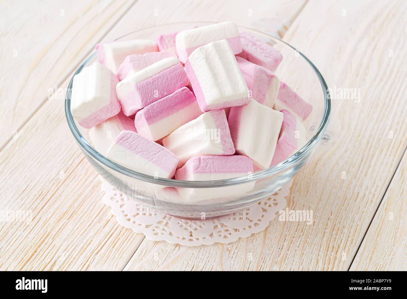 Blanc Rose fluffy les guimauves dans un bol en verre sur une table en bois. Hiver doux et savoureux de la nourriture. Close-up de délicieux bonbons mous. Vue de face. Banque D'Images