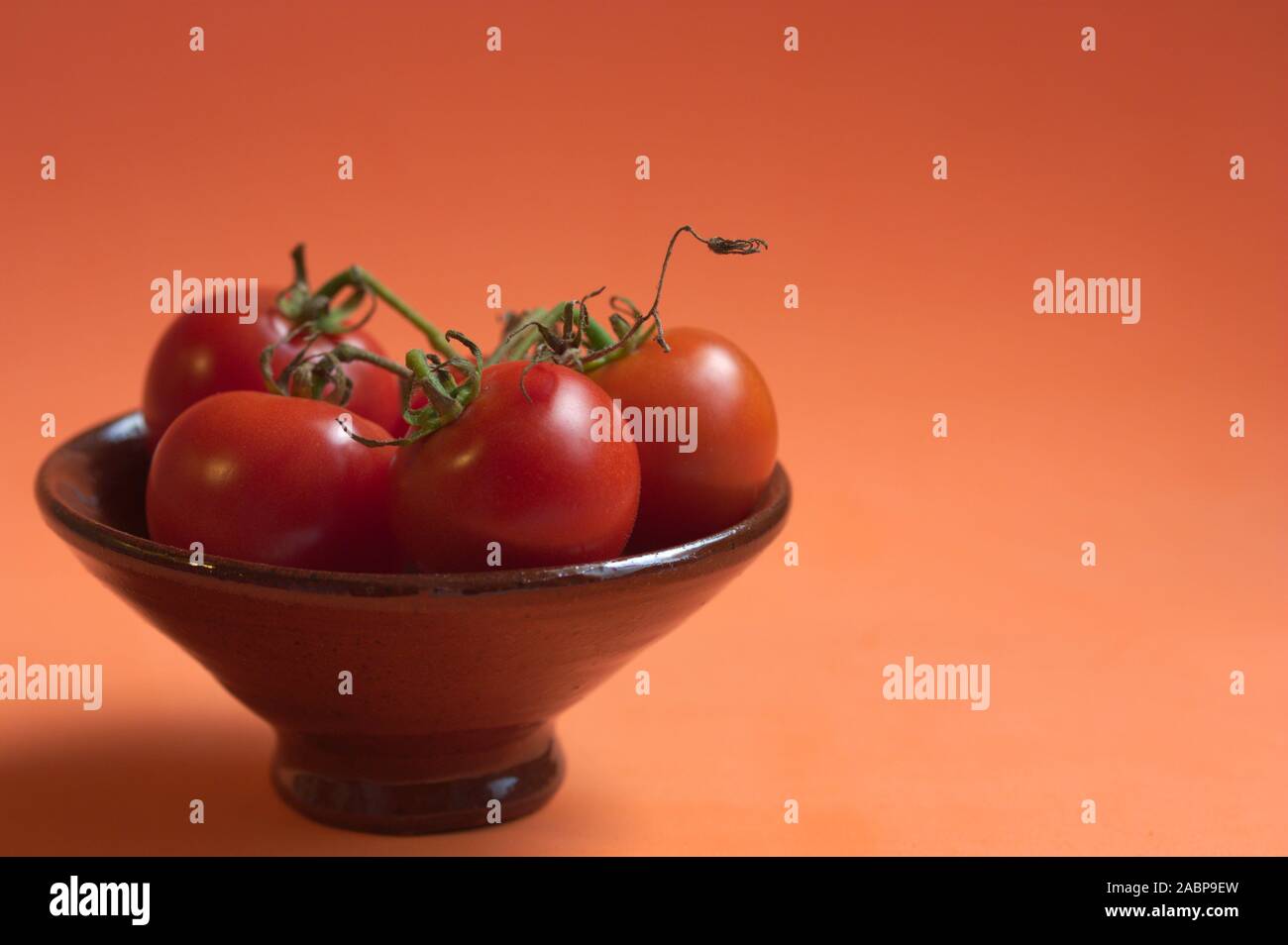 Un bol brun avec quelques tomates cerises sur branch sur fond orange et de l'espace pour la copie des textes (l'espace) Banque D'Images
