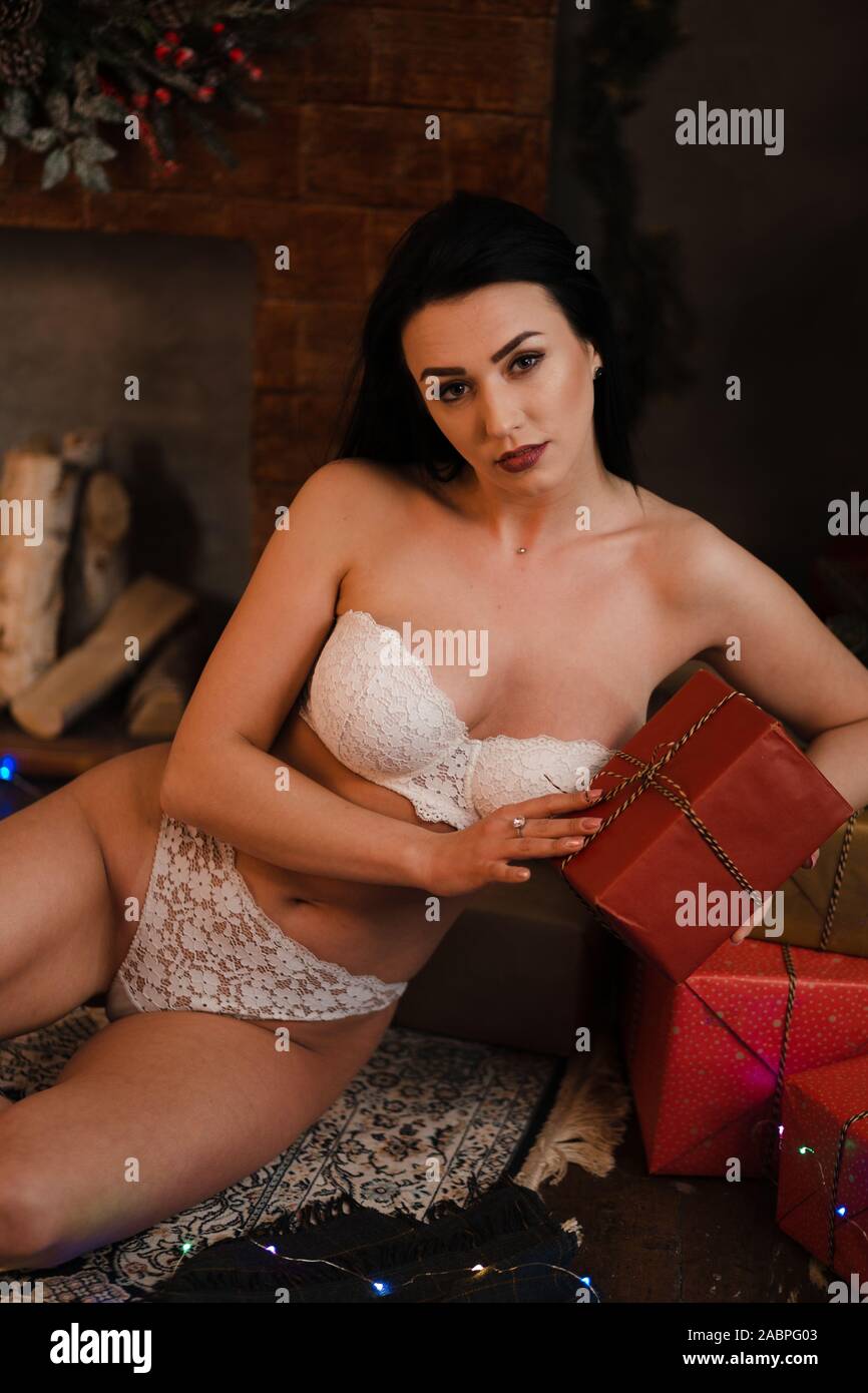 Femme en lingerie s'assied à un arbre de Noël et une fausse cheminée holding xmas trouble - Sexy et chaud en sous-vêtements blancs colorés avec garland en l Banque D'Images