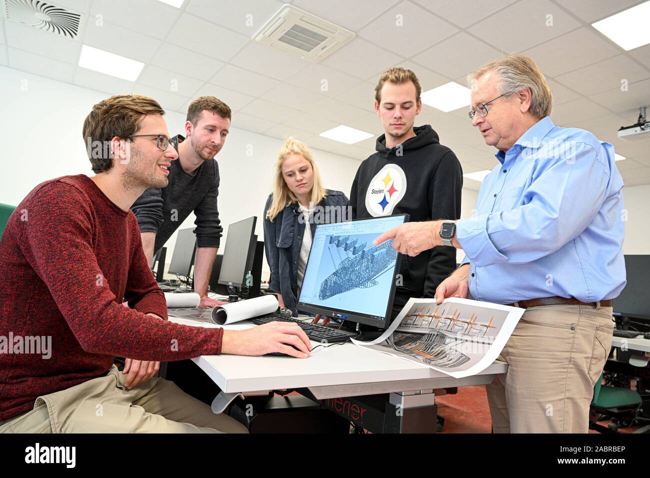 Friedrichshafen, Allemagne. 27 Nov, 2019. Ingénieur et informaticien Peter Kielhorn (r) est titulaire d'une vue de côté de l'hydravion n'X à la main, pendant que les élèves Dominik Bodenmüller (l-r) Kai Peter, Sofia Stich et Pascal Mannig travailler sur l'ordinateur. Le 12 juillet 2029, une réplique exacte du célèbre Dornier Do X Flying Boat est érigé à Friedrichshafen sur le lac de Constance - sur le 100e anniversaire du premier vol de l'avion. Crédit : Felix Kästle/dpa/Alamy Live News Banque D'Images