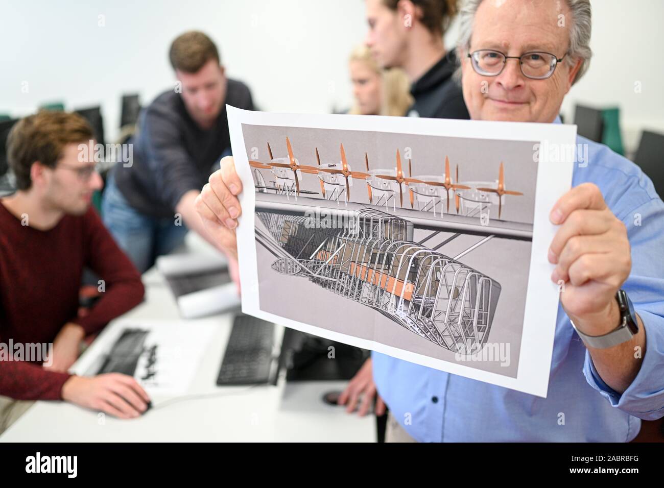 Friedrichshafen, Allemagne. 27 Nov, 2019. Ingénieur et informaticien Peter Kielhorn (r) est titulaire d'une vue de côté de l'hydravion n'X, tandis que les étudiants Dominik Bodenmüller (l-r), Kai Pete, Sofia Stich et Pascal Mannig travailler sur l'ordinateur en arrière-plan. Le 12 juillet 2029, une réplique exacte du célèbre Dornier Do X Flying Boat est érigé à Friedrichshafen sur le lac de Constance - sur le 100e anniversaire du premier vol de l'avion. Crédit : Felix Kästle/dpa/Alamy Live News Banque D'Images