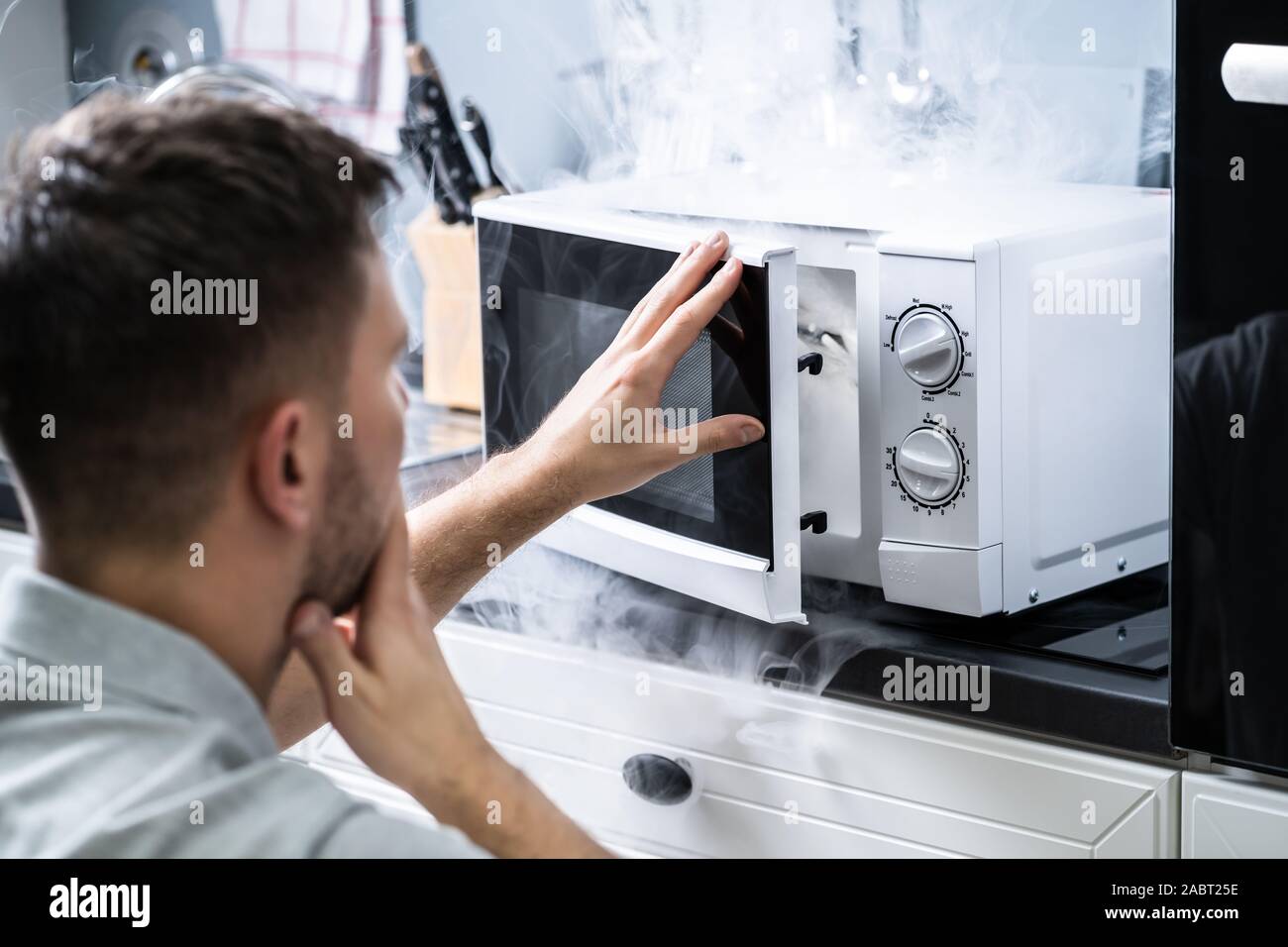 Jeune homme pulvérisant extincteur sur le four à micro-ondes dans la cuisine Banque D'Images