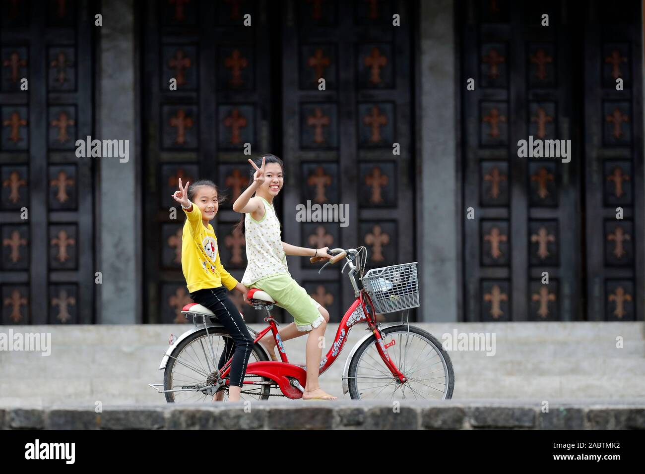 Phu Cam cathédrale. Deux jeunes filles d'une bicyclette faisant le signe V. Hue. Le Vietnam. Banque D'Images