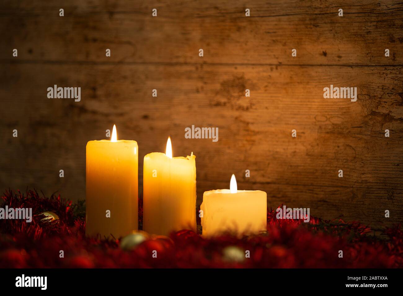 La chaleur de la notion de Noël : trois chandelles allumées sur une table en bois clair et un cadre rustique avec des branches de pins, décoration rouge et or et re Banque D'Images