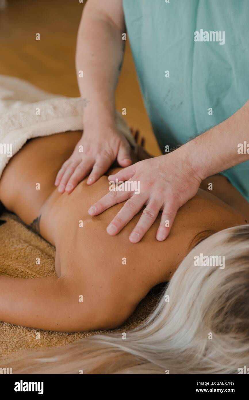 Blonde woman relaxing massage dos récepteur par un homme de la physiothérapeute en instituts de beauté allongée sur table de massage. Jeune fille avec des tatouages à spa détente Banque D'Images