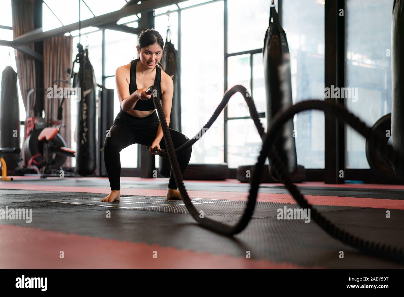 Belle femme asiatique avec balck corde bataille bataille des cordes de l'exercice dans la salle de remise en forme avec sac de boxe en arrière-plan. S'adapter aux modes de vie sportive Banque D'Images