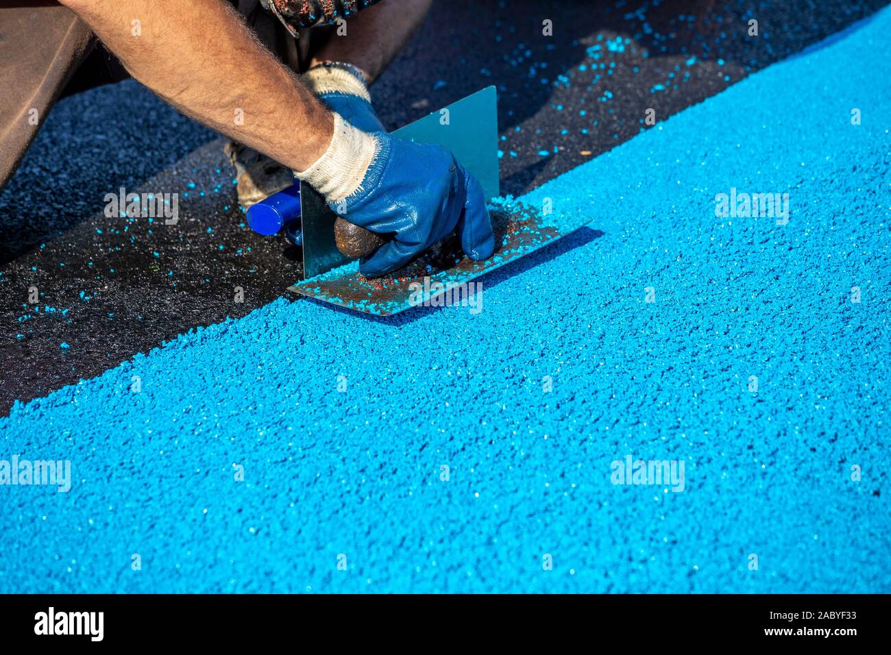 Revêtement en caoutchouc artificiel de mise à niveau de Mason pour les terrains de jeux et sports, appliqué sur la surface par un acier de truelles. Granulés de caoutchouc de MPD. Focus sélectif. Banque D'Images