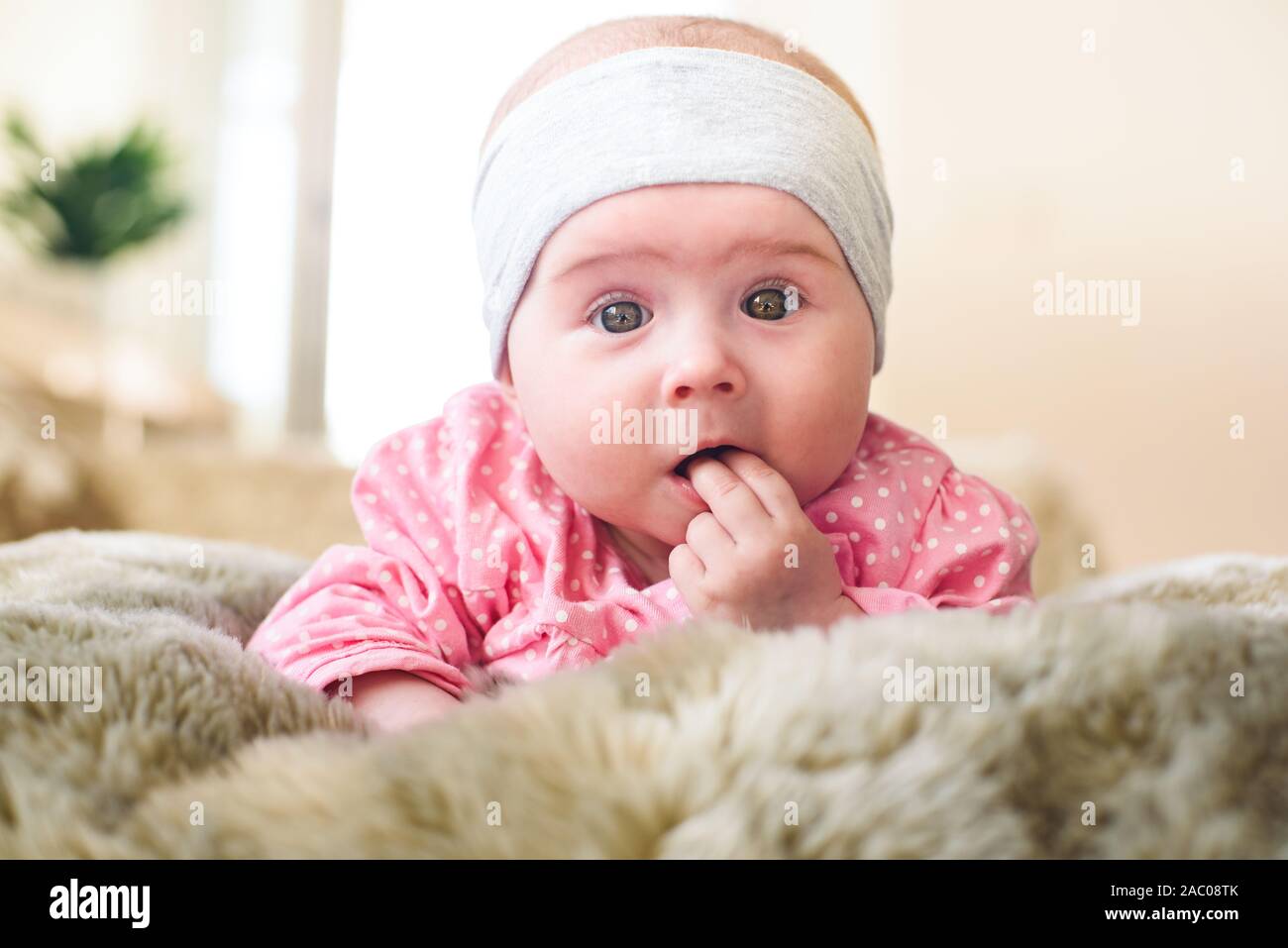Jolie Petite Fille De 6 Mois Sur Un Lit Bebe Sur Son Ventre Avec La Tete Relevee Et Les Doigts Dans La Bouche A La Recherche Vers La Camera Avec Ses Grands