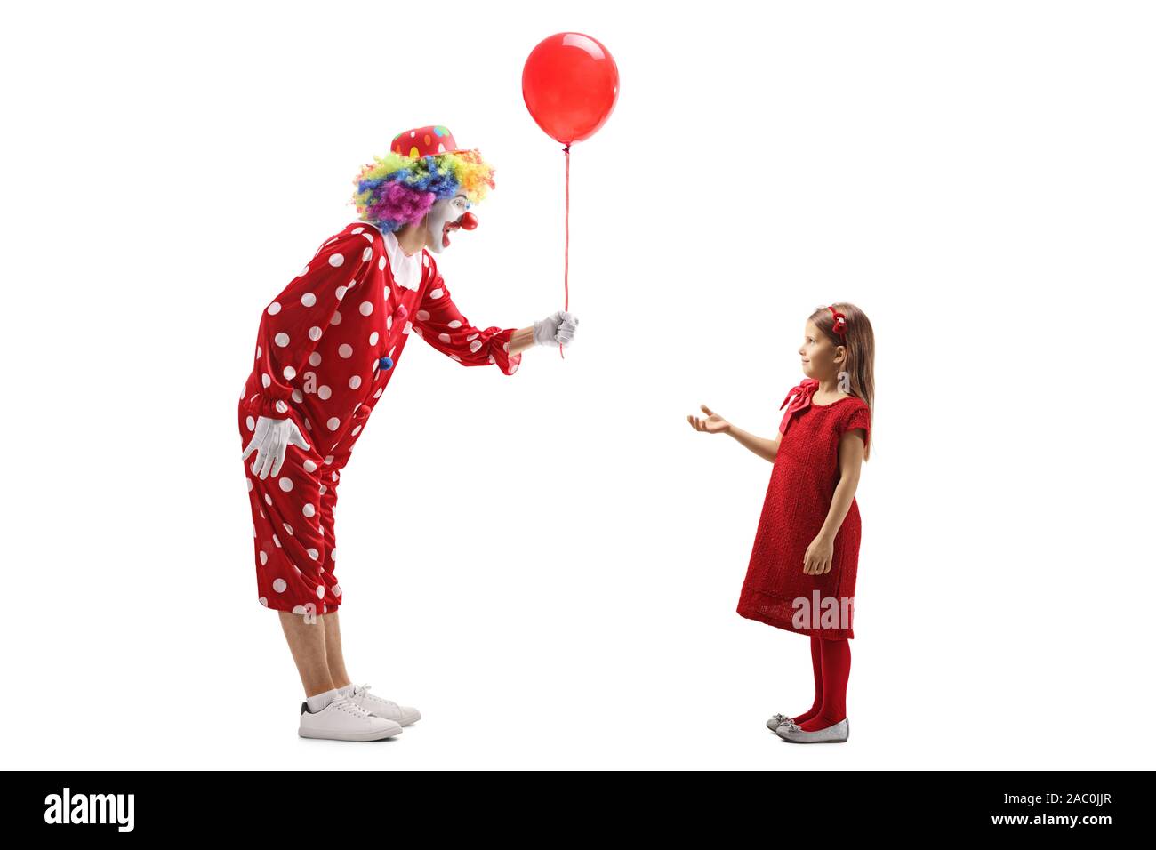 De toute la longueur d'un clown en donnant un ballon rouge pour une petite fille isolée sur fond blanc Banque D'Images