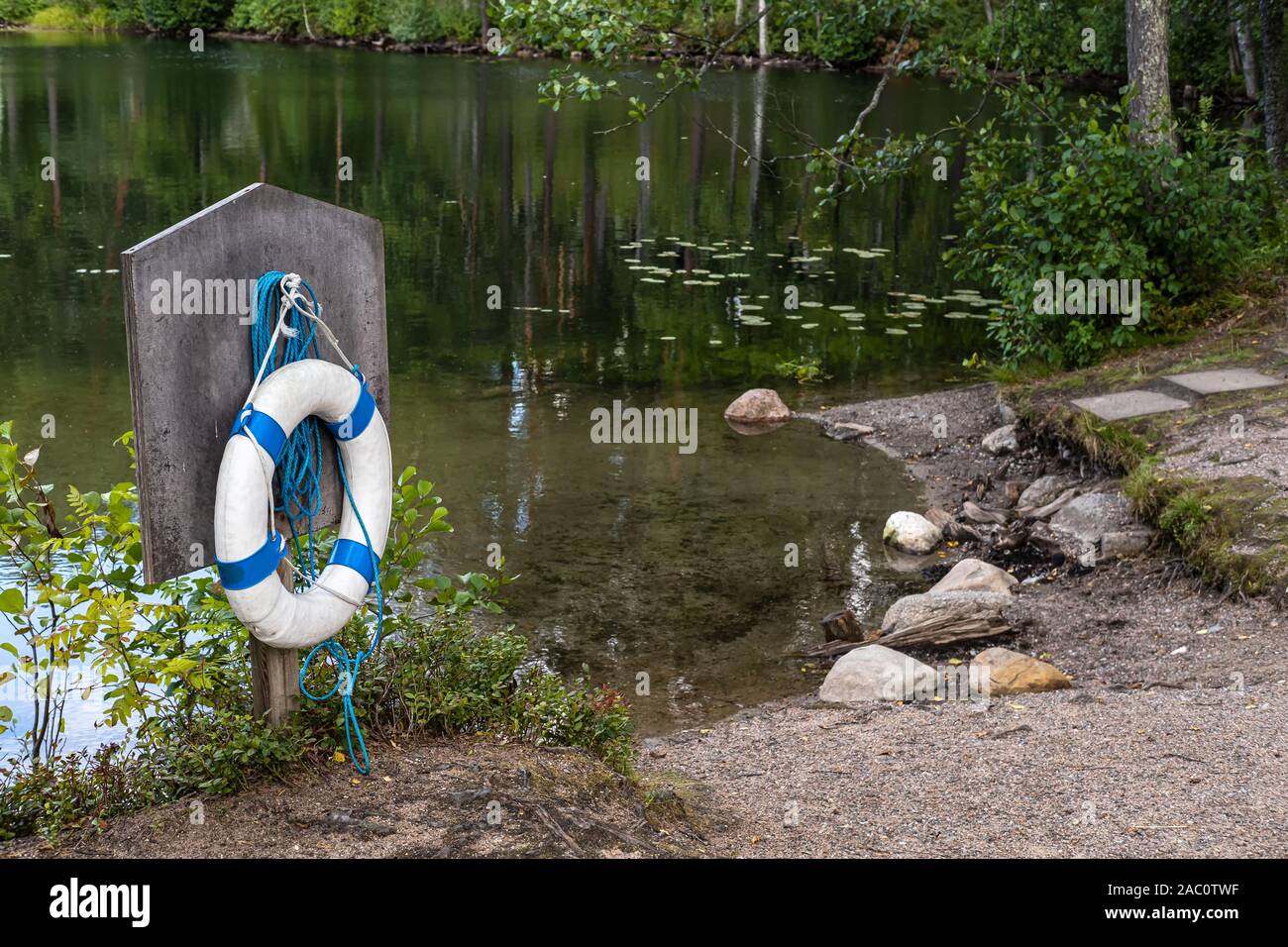 Bouée de sauvetage et d'une corde sont accrochés sur un conseil spécial, sur le bord d'une magnifique forêt, lac dans lequel se reflètent les arbres. Vacances en toute sécurité concept. Banque D'Images
