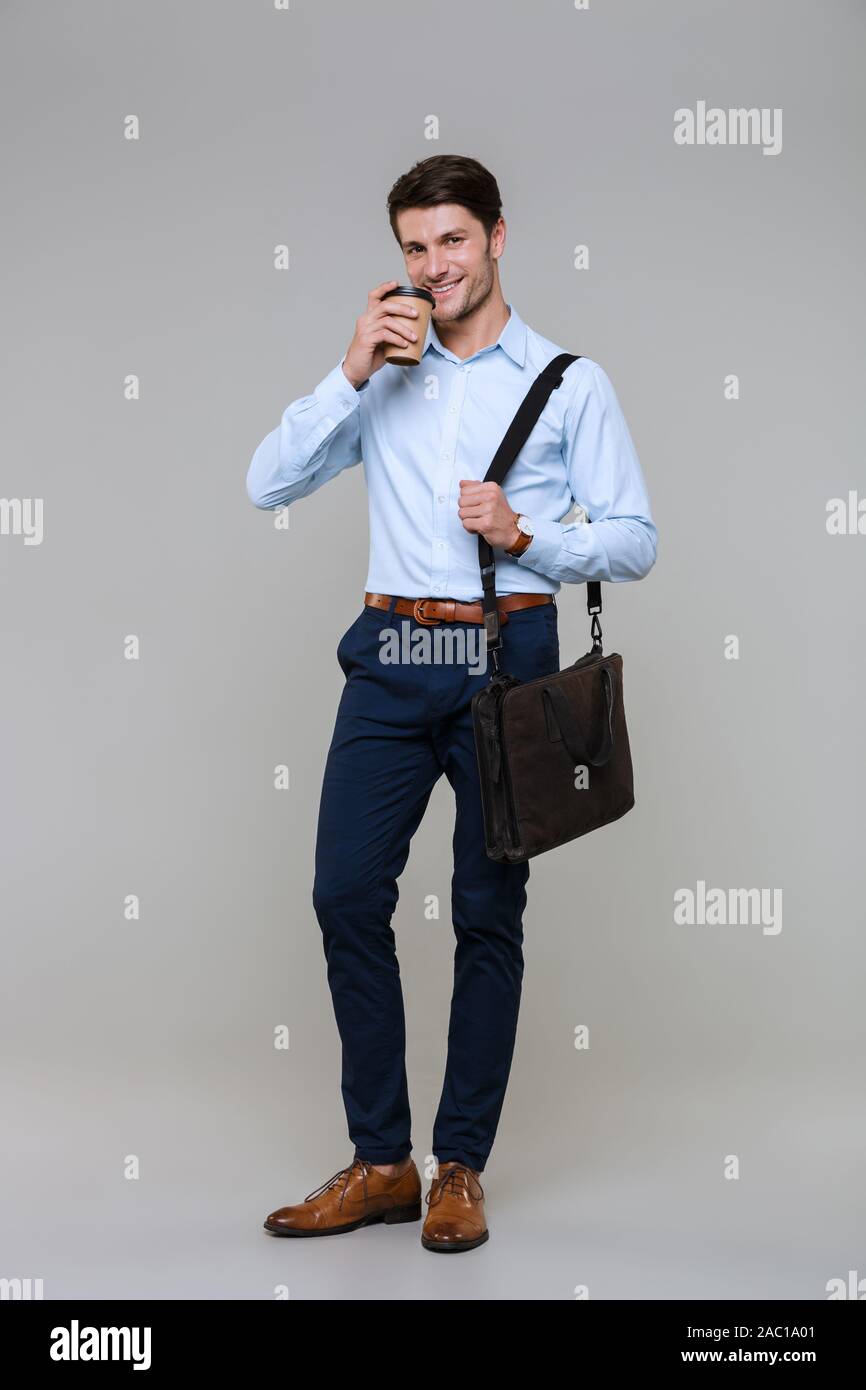 Full Length portrait of smiling businessman in office clothes holding Coffee cup et isolé dans un sac d'ordinateur portable sur fond gris Banque D'Images