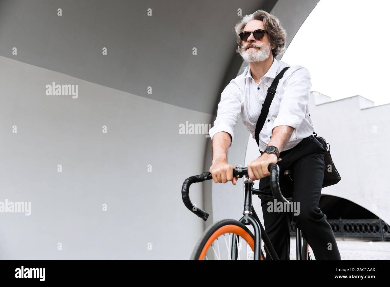 Photo de confiance mature businessman en lunettes de soleil et chemise blanche riding bicycle on city street Banque D'Images