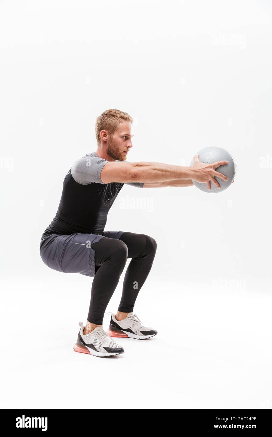 Certain beau jeune sportif fit faire les exercices avec fitness ball isolated over white background, accroupie Banque D'Images