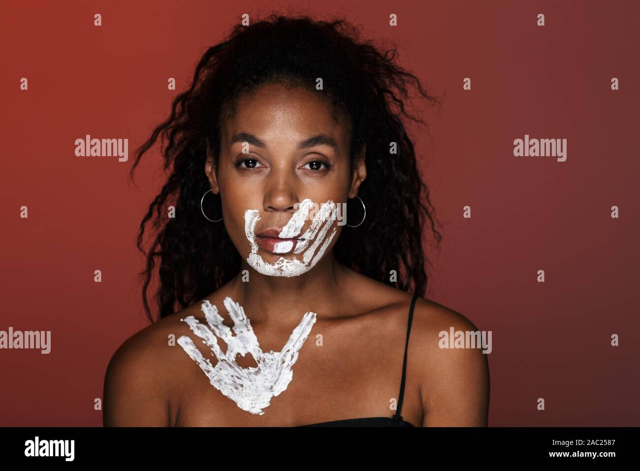 Image d'une jeune femme africaine sérieuse isolated over red wall background with Hand Print sur le visage et clavicules. Banque D'Images