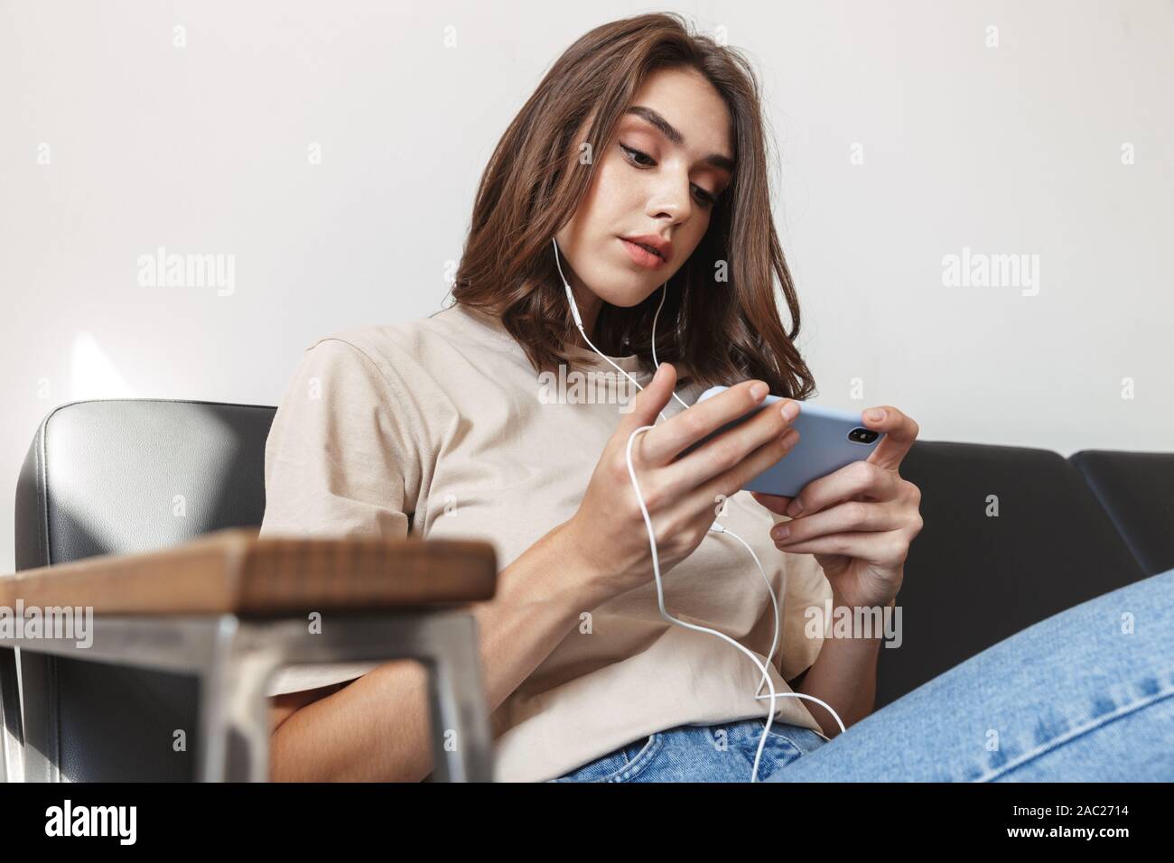 Image de la belle jeune femme portant des écouteurs d'écouter de la musique sur smartphone dans l'appartement Banque D'Images