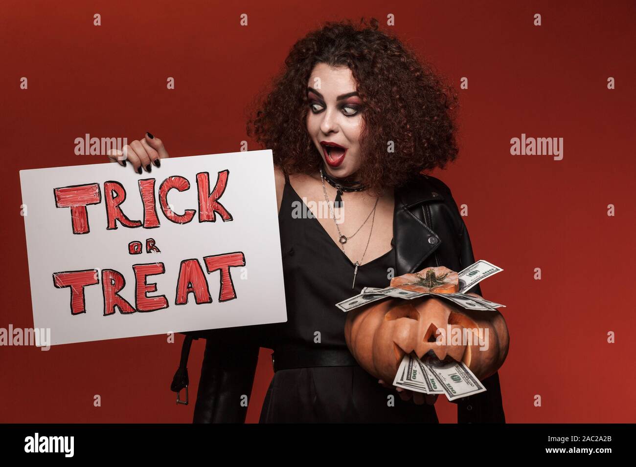 Image de sorcière excité girl holding halloween citrouille et trick ou traiter les plus isolés du mur rouge Banque D'Images