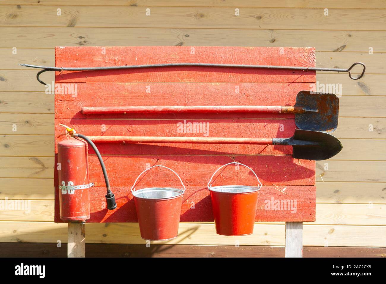 Ensemble d'appareils de sécurité incendie rouge sur planche de bois. extincteur, seau, pelle et ferraille. Banque D'Images