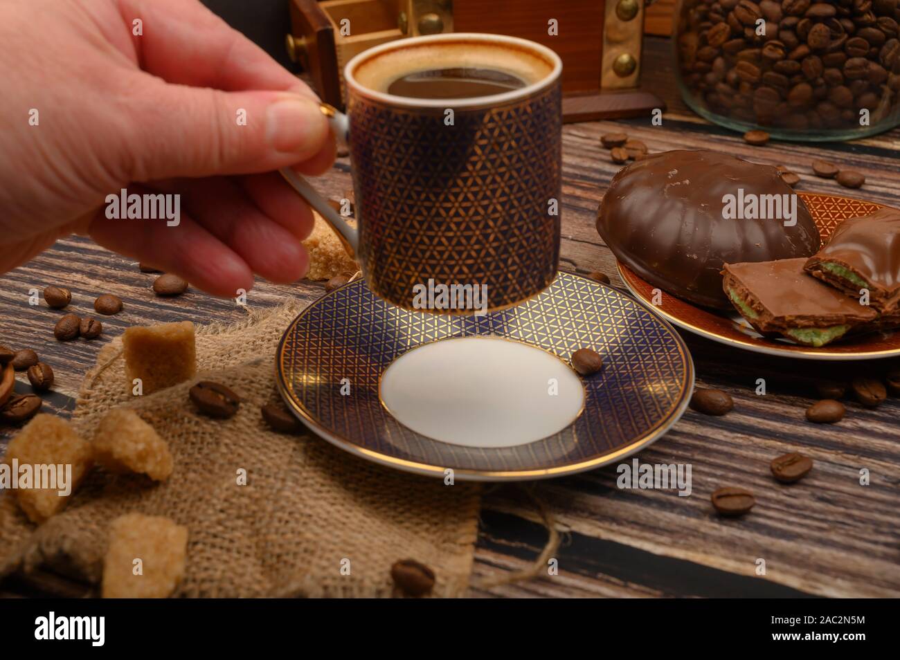 La main de la jeune fille tient une tasse de café sur une table en bois avec le sucre brun, les grains de café et chocolat Banque D'Images