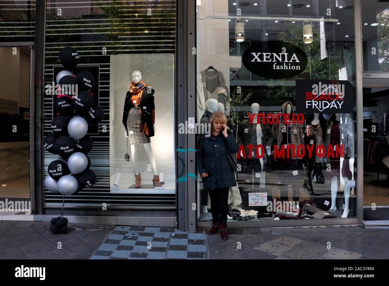 Une femme se tient à l'extérieur d'une boutique tout en parlant au téléphone pendant la vente Vendredi Noir.à certains magasins à Athènes, les ventes n'attendez pas pour le vendredi pour arriver. Les magasins ouverts à partir du jeudi soir bien que certains magasins prennent position contre le début d'une action de coupe courte. Banque D'Images