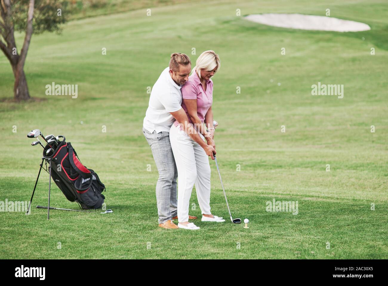 L'enseignement de l'homme femme à jouer au golf sur le terrain de sport avec équipement derrière Banque D'Images