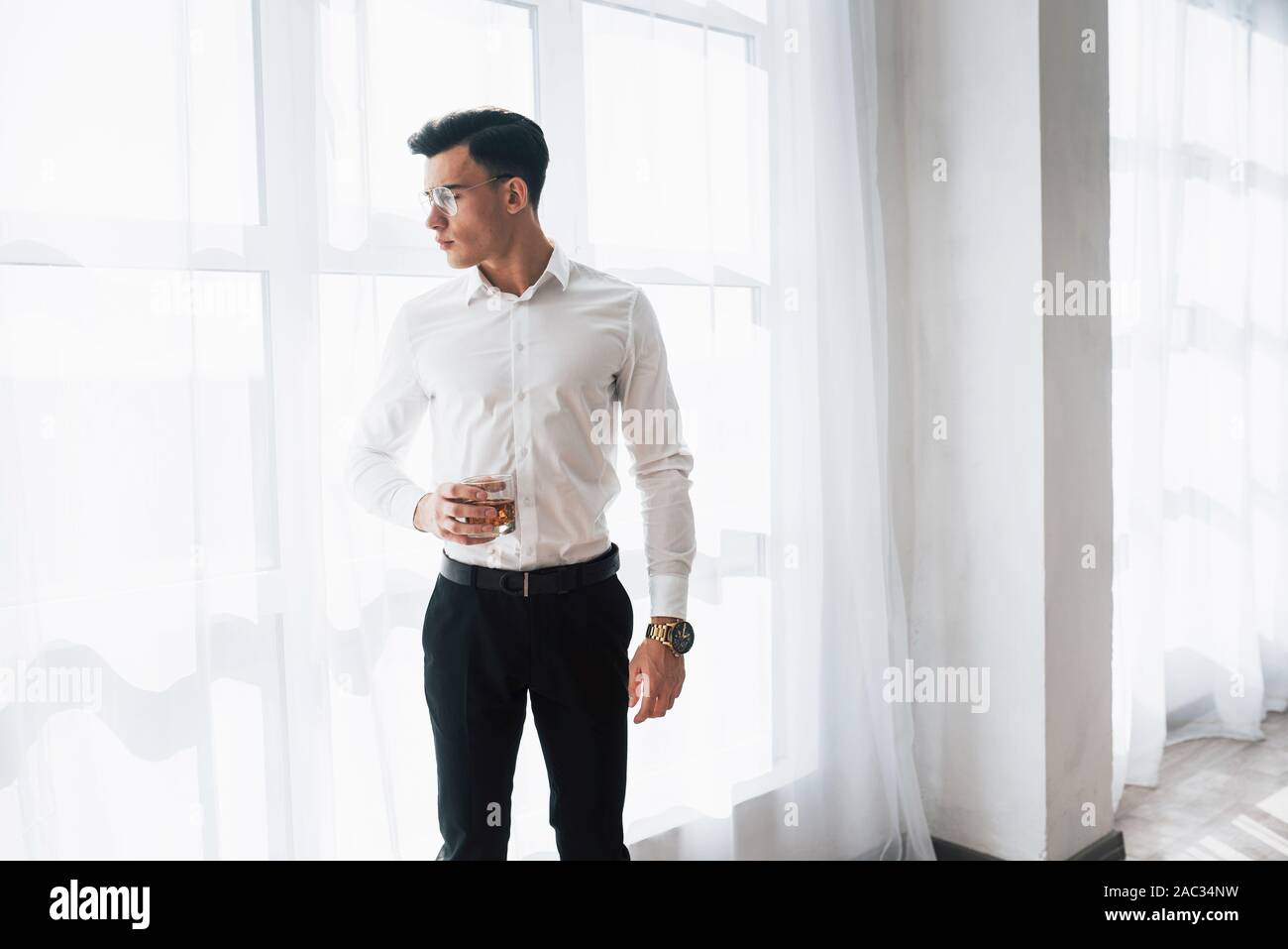 Homme splendide dans les lunettes et intérieur stand détenteur de l'alcool Banque D'Images