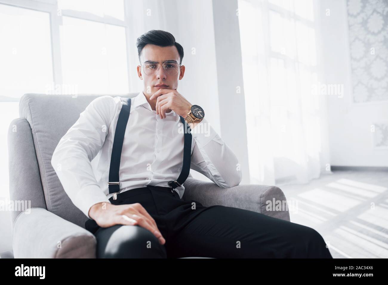 La photo en gros plan de guy attrayant dans les verres et élégant porter assis sur la chaise Banque D'Images