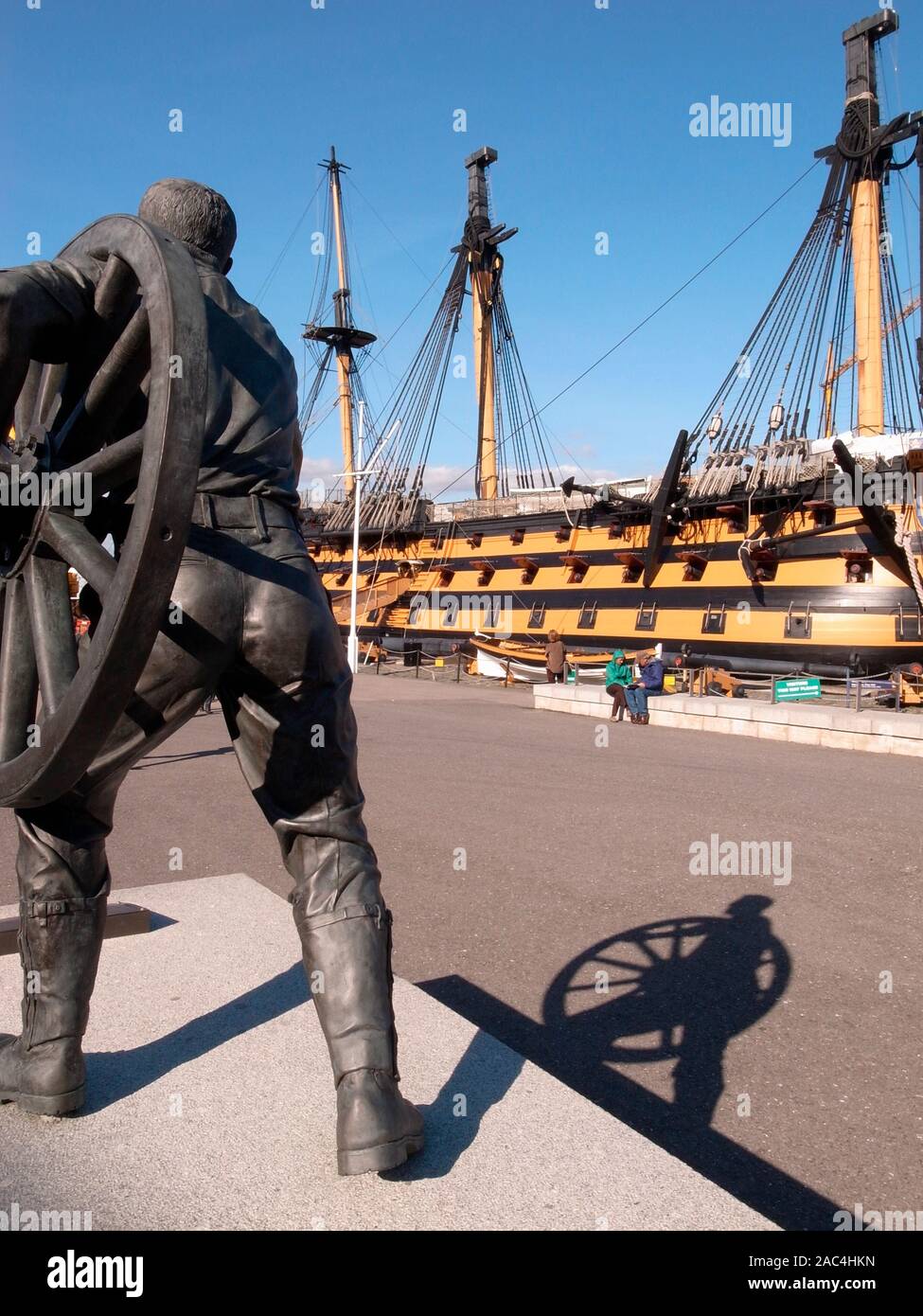 AJAXNETPHOTO. PORTSMOUTH, Angleterre. - Chantier naval HISTORIQUE STATUE EN BRONZE - UN CHAMP GUNNER REPRÉSENTÉ TRANSPORTER UNE ROUE DE CANON DE CAMPAGNE PAR SCULPTEUR BRITANNIQUE CHRISTOPHER KELLY. La STATUE SUR UN SOCLE COMMÉMORE LES HOMMES DE PORTSMOUTH DANS LE CANON DE CAMPAGNE ANNUELLE DE LA CONCURRENCE AU TOURNOI ROYAL ET QUI SE SONT ENTRAÎNÉS À LA CASERNE DE LA MARINE ROYALE DE 1947-1999 LORSQUE LE TOURNOI EST TERMINÉ. À LA LIMITE ET AU-DELÀ. NELSON'S 1805 BATAILLE DE TRAFALGAR NAVIRE AMIRAL HMS Victory est vu l'arrière-plan. PHOTO:JONATHAN EASTLAND/AJAX REF:GR110111_3170 Banque D'Images