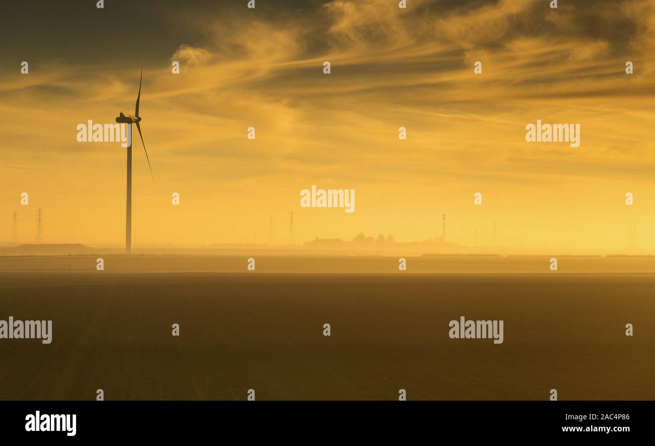 Seule éolienne capturé au lever du soleil dans la campagne de France avec silhouettte de poteaux d'électricité à la base. Banque D'Images