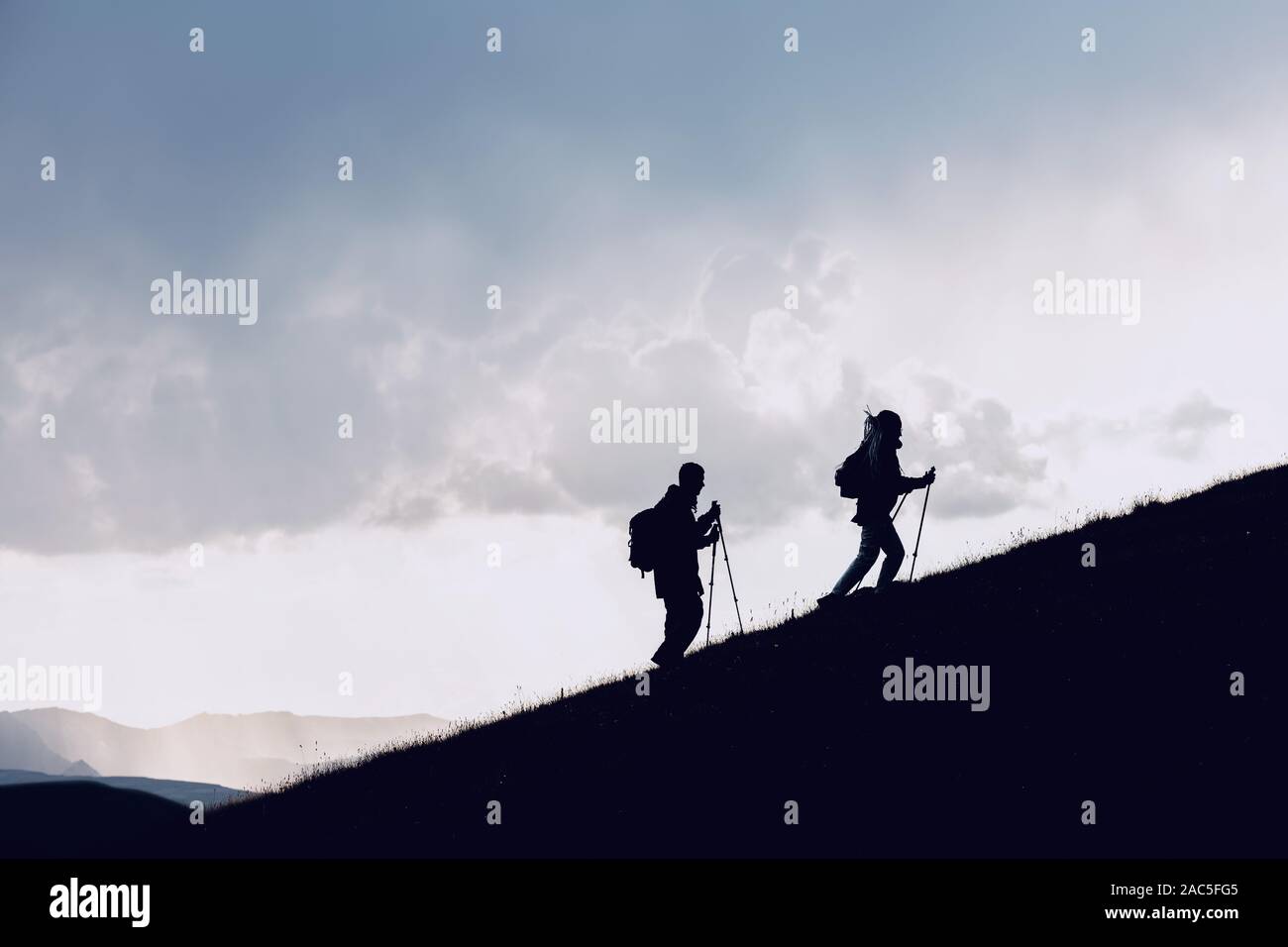 Deux silhouettes s'accompagne en amont les randonneurs en montagne contre nuages Banque D'Images