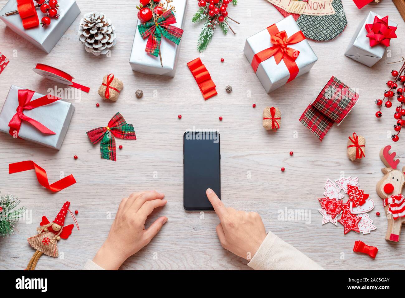 Smart phone sur table en bois entourée de décorations de Noël. Girl touch téléphone affichage vierge. Mise à plat, vue supérieure de la composition. Banque D'Images