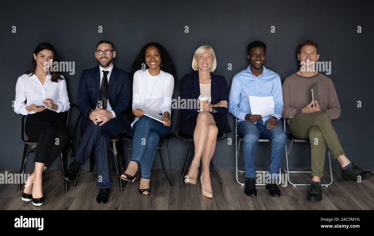 Divers pleine longueur smiling business people sitting in line sur des chaises. Banque D'Images