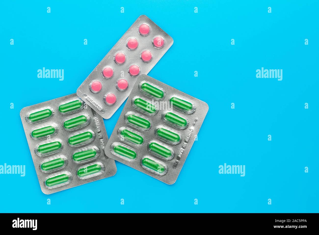 Distributeur de pilules sur un fond bleu. Copier l'espace. Blisters de comprimés roses et verts de capsules. Concept de la médecine. Banque D'Images