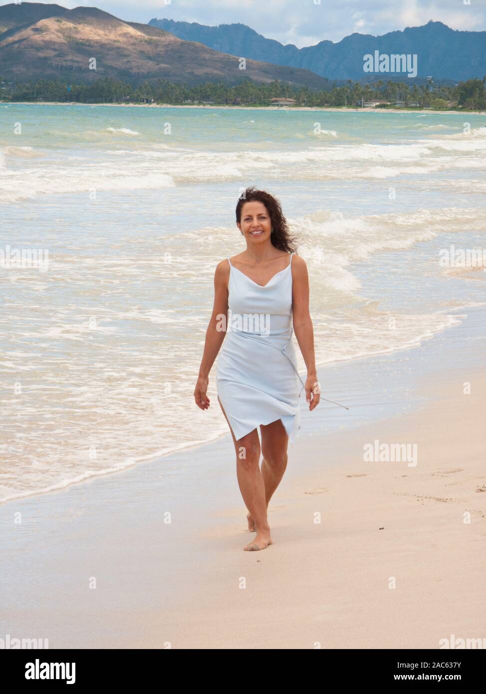 Femme marche Kailua beach avec des cheveux bouclés portant robe bleu clair Banque D'Images