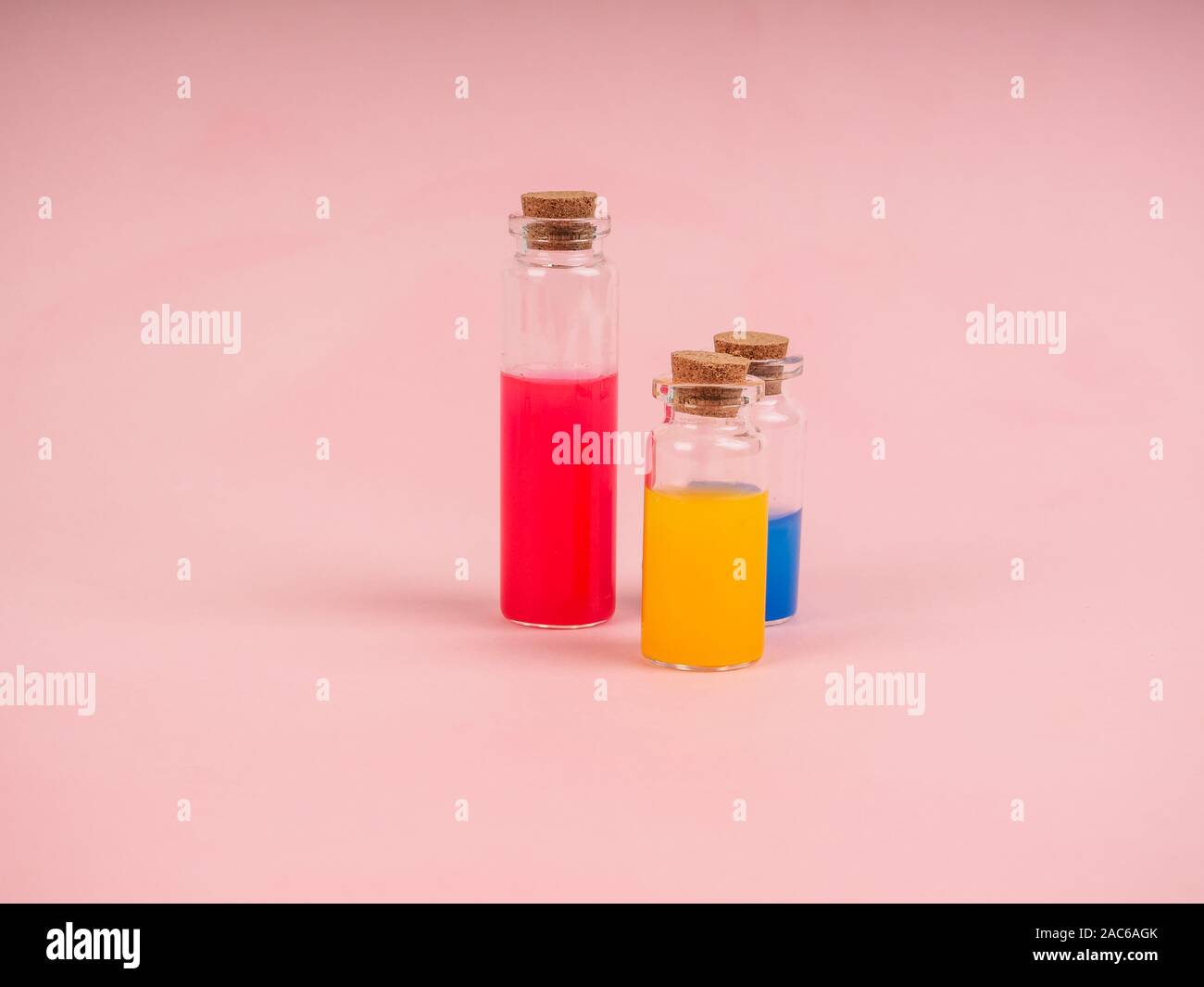 Fleurs et extraits de plantes ou parfum dans de petites bouteilles sur fond rose. Trois petites bulles avec du liquide rouge bleu et jaune, le concept de Banque D'Images