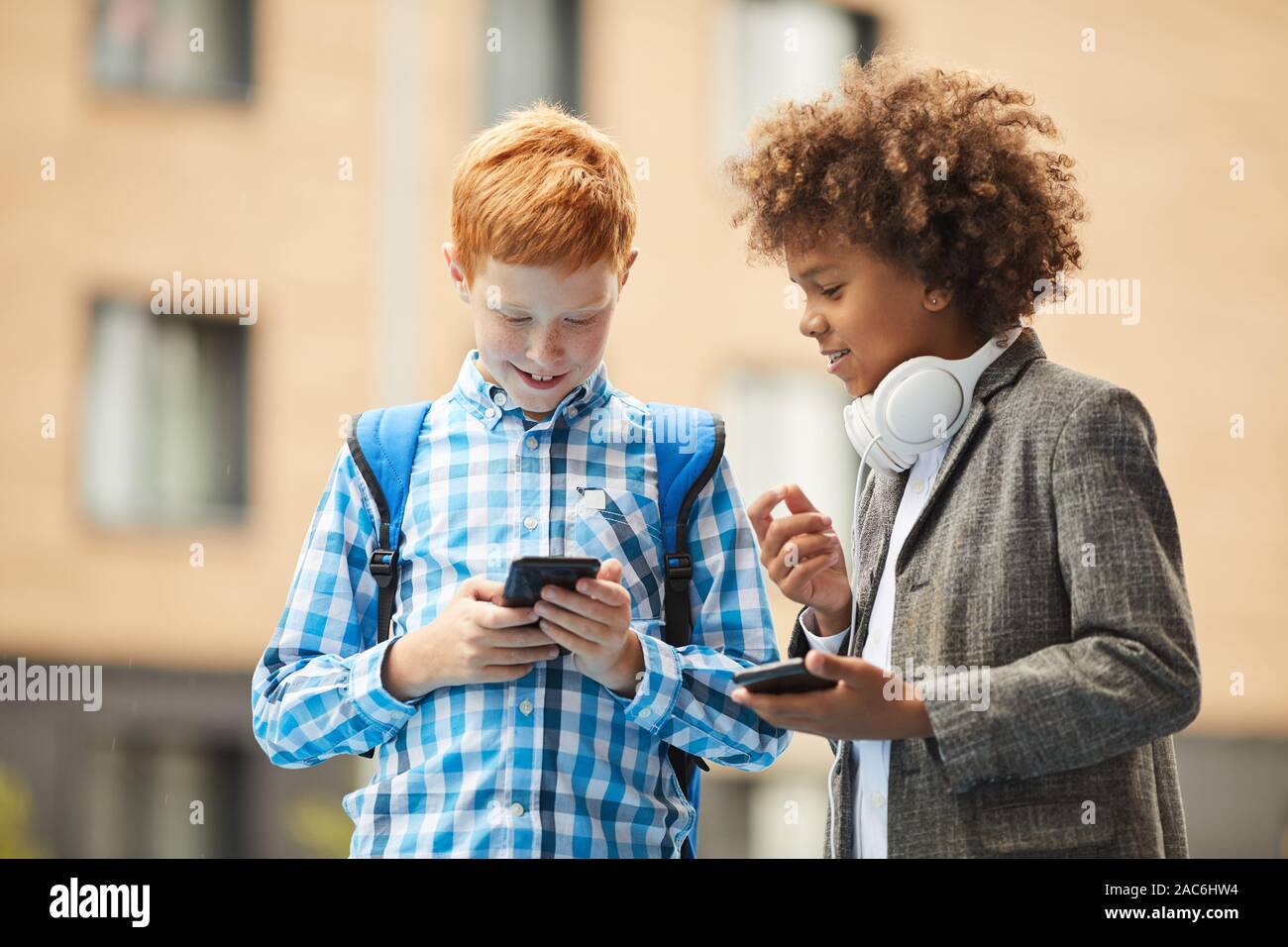 Deux garçons debout avec les téléphones mobiles aborder quelque chose et étudier en ligne à l'extérieur Banque D'Images
