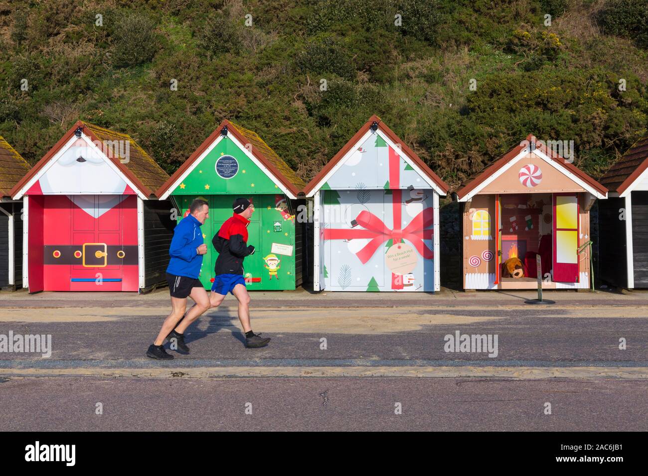 Bournemouth, Dorset UK. 1er décembre 2019. Cabines de plage obtenir leurs manteaux sur Noël à la plage de Bournemouth, décorée comme épice, Père Noël, cadeau de Noël et Elf avec la possibilité d'aller à l'intérieur de l'un d'épice de prendre des autoportraits avec un décor accueillant sur une journée ensoleillée à sec, mais très froid. Les coureurs courent le long de la promenade au-delà de la plage de Noël des huttes. Credit : Carolyn Jenkins/Alamy Live News Banque D'Images