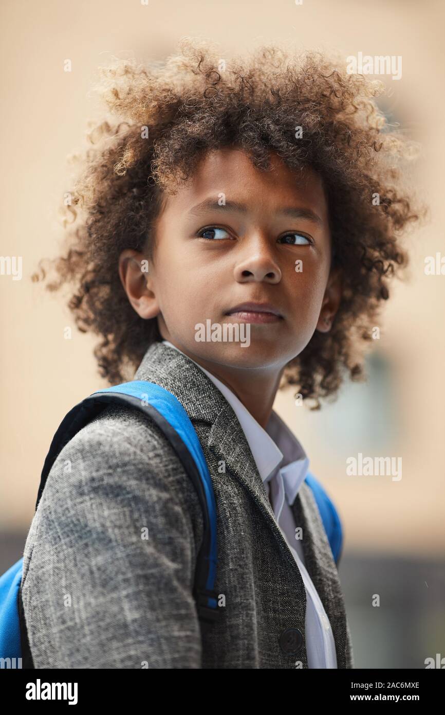 Écolier africain avec des cheveux bouclés et avec sac à dos derrière son dos à l'extérieur et à l'écart permanent Banque D'Images