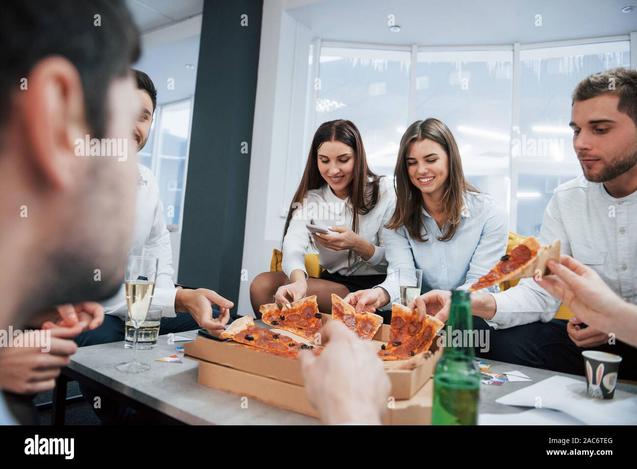 Avoir du bon temps. Manger des pizzas. La célébration de traiter avec succès. Les jeunes travailleurs de bureau assis près de la table avec de l'alcool Banque D'Images