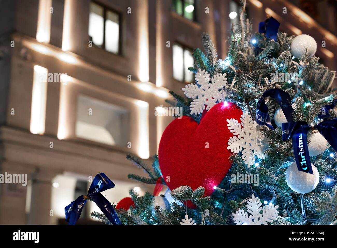 Un arbre de Noël décoré avec un cœur rouge, rubans bleus, flocons et boules blanches Banque D'Images