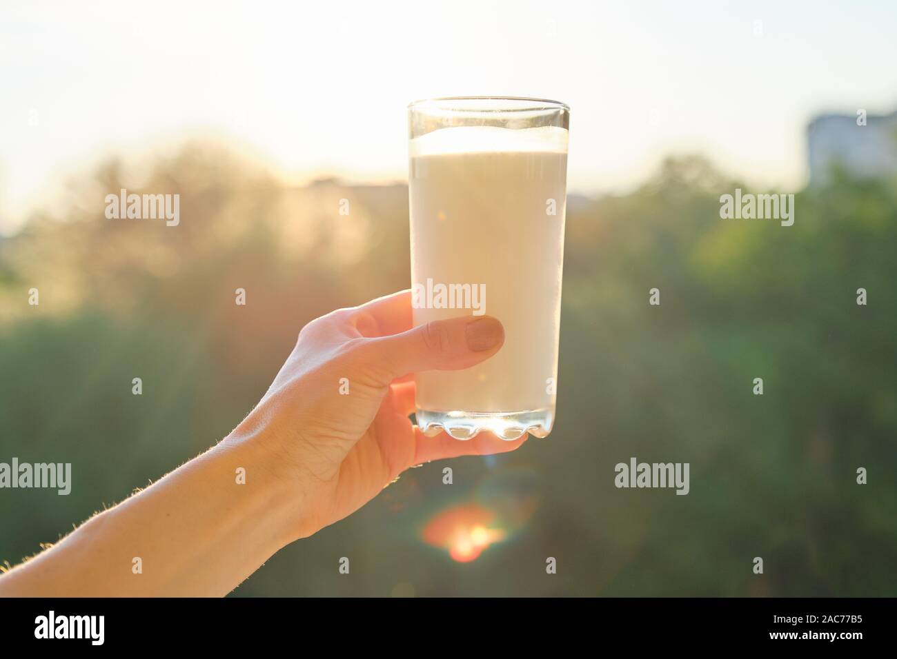 Avec le verre de lait dans la main de femme, l'arrière-plan le coucher du soleil, soir, ville Banque D'Images