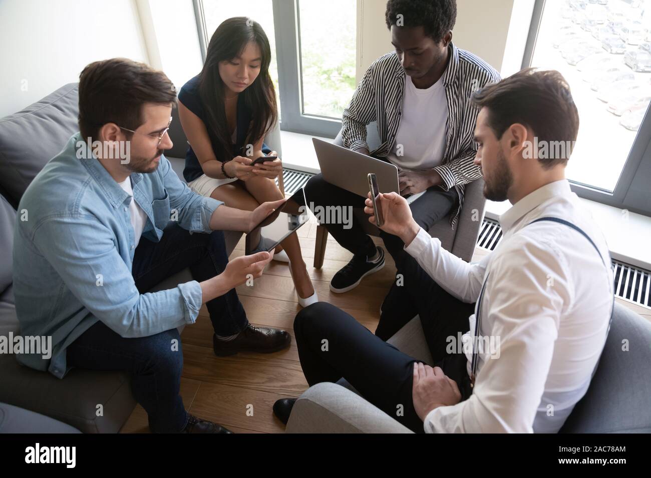 Les travailleurs multiethnique assis en cercle en utilisant divers gadgets mobiles Banque D'Images