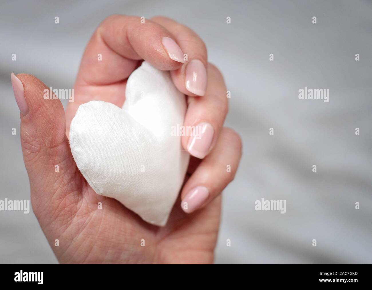 Artisanal blanc coeur dans la main de femme sur fond gris. L'amour, l'espoir, concept de don. Banque D'Images