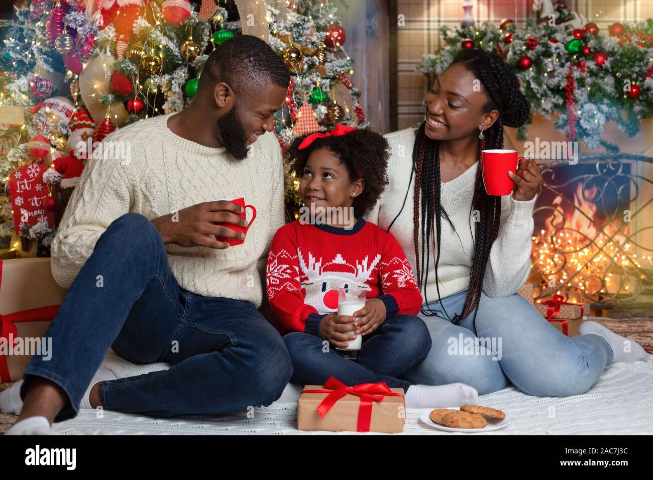 Cheerful famille africaine de manger des collations et boire du lait près de l'arbre de Noël Banque D'Images