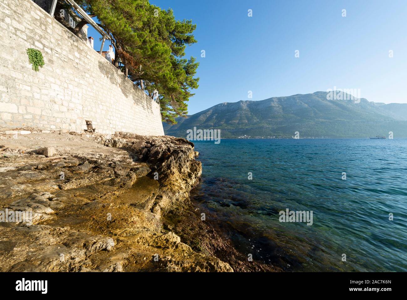 Roches sur l'eau en dessous du mur de la ville de Korcula avec vue sur la mer et les montagnes de Peljesac, Dalmatie, Croatie Banque D'Images