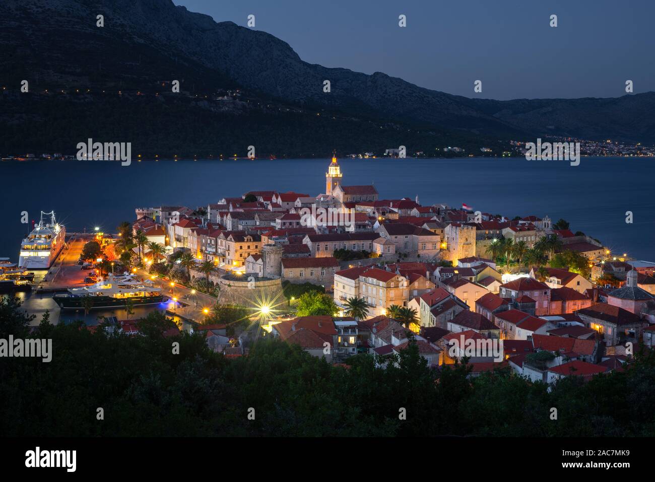 Vue sur les rues médiévales et les bâtiments de la vieille ville historique de Korcula en face de l'île de Peljesac après le coucher du soleil dans l'heure bleue Banque D'Images